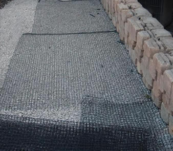 Biaxial plastic geogrid is covering the gravel and some large stone is on the geogrid.