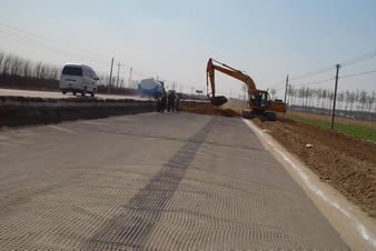 The biaxial plastic geogrid is covering the road and an excavator is laying the soil on the ground.