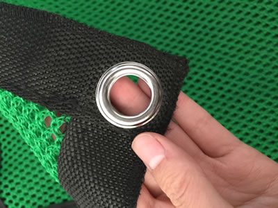A hand is holding the metal button hole of flexible windbreak netting.