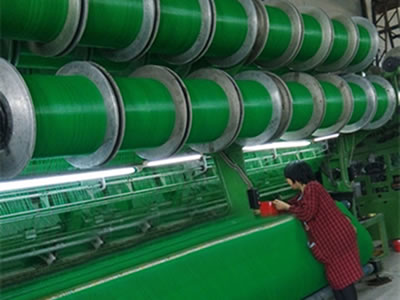 A machine is producing green color flexible windbreak netting and a roll of netting on the ground.
