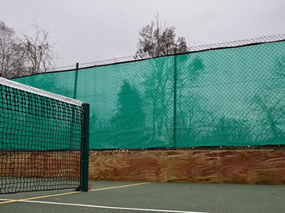 Green color flexible windbreak netting is attached onto the chain link fencing of tennis court.