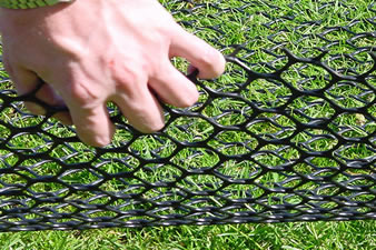 A hand is holding a part of hexagonal grass protection mesh, which is covering the grassland.