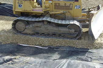 Quaxial plastic geogrid is installed on the geotextile and a bulldozer is paving the gravels.