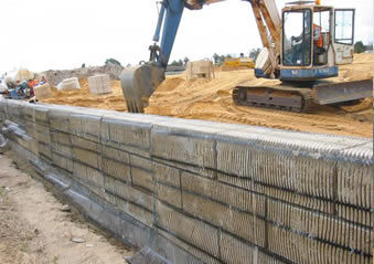 Uniaxial plastic geogrid is covering the retaining wall and an excavator is working.