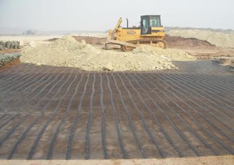 Uniaxial plastic geogrid is covering the ground and a bulldozer is laying the soil on the road.