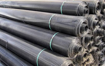 Several rolls of uniaxial plastic geogrid are placed on the ground.